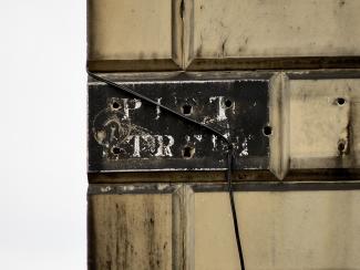 Faded street-name sign attached to masonry. White letters on black background reading PITT STREET.