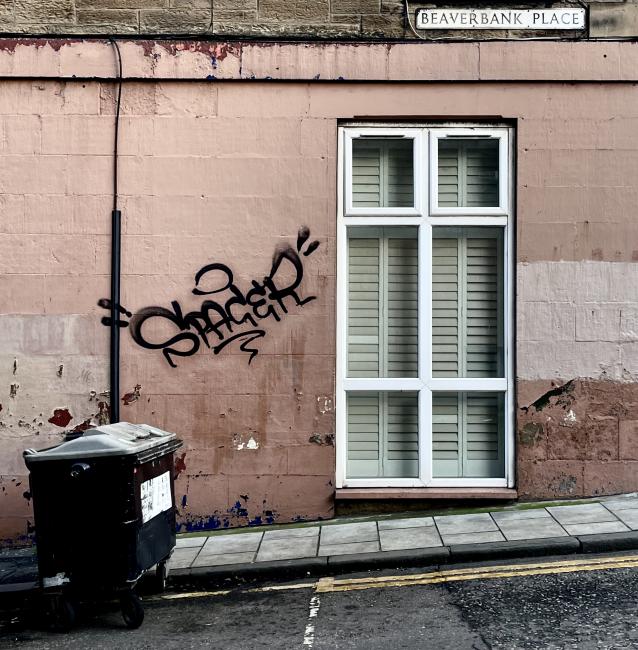 Sloping footway, red masonry with graffiti, and street-level window on Beaverbank Place.