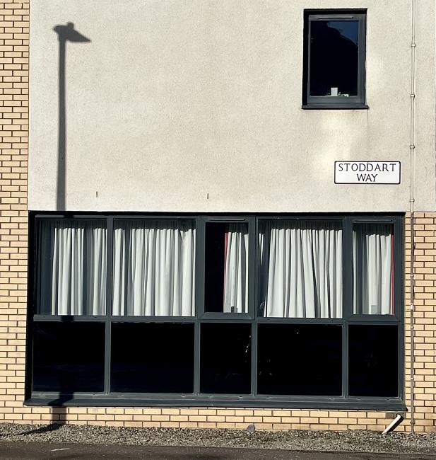 Shadow of a lamppost on Stoddart Way wall, resembling a giraffe's neck and head.